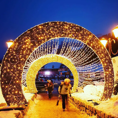 A walk-through tunnel decoration with pre-lit LED lights designed for holiday displays, with people visible walking through the tunnel.