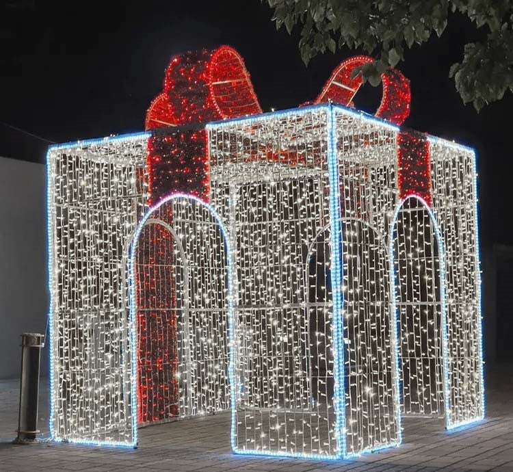 A large, walk-through gift box decoration made of metal frames with white and red LED lights, intended for holiday decorations.